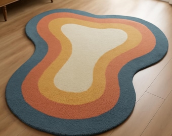 Könnte beinhalten: Ein Teppich im Retro-Stil mit einer einzigartigen, organischen Form. Der Teppich hat konzentrische Farbstreifen, darunter Creme, Gelb, Orange und einen tiefblauen Rand. Der Teppich besteht aus einem weichen, strukturierten Material.