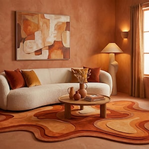 May include: A living room featuring a cream sofa, orange and brown cushions, and a round wooden coffee table. An abstract painting hangs above the sofa. The floor is covered by an organic-shaped rug in shades of orange and brown.
