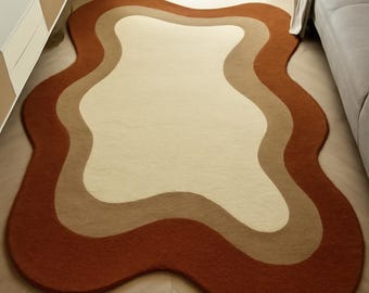May include: A unique, wavy-edged rug in a bedroom setting. The rug features a layered design with shades of beige, tan, and rust-orange. The rug's shape and color palette create a warm and inviting atmosphere, suitable for a living space.