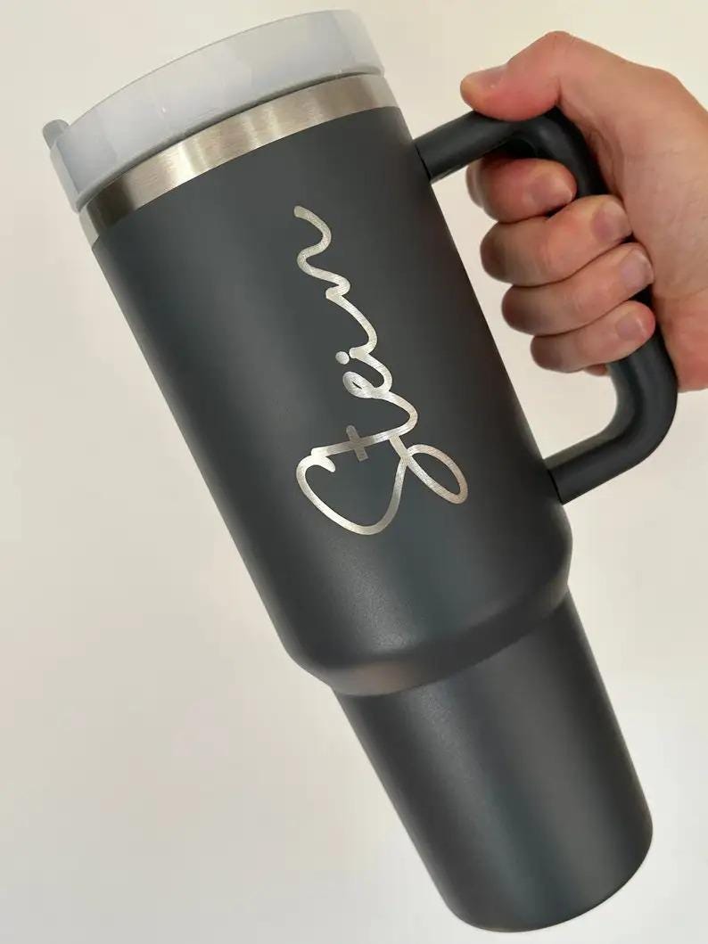 Op de afbeelding: Een donkergrijze ge&iuml;soleerde beker met een handvat, een zilveren rand en een wit deksel. De naam "Erin" staat in zilveren letters op de zijkant. Ontworpen om dranken warm of koud te houden.