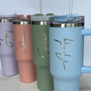 Op de afbeelding: Vier ge&iuml;soleerde bekers in pastelkleuren: lavendel, perzik, saliegroen en lichtblauw. Elke beker heeft een zilveren deksel, een handvat en een naam in cursief. Er zitten doorzichtige rietjes in.