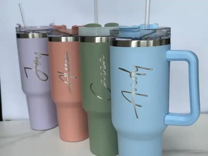 Op de afbeelding: Vier ge&iuml;soleerde bekers in pastelkleuren: lavendel, perzik, saliegroen en lichtblauw. Elke beker heeft een zilveren deksel, een handvat en een naam in cursief. Er zitten doorzichtige rietjes in.