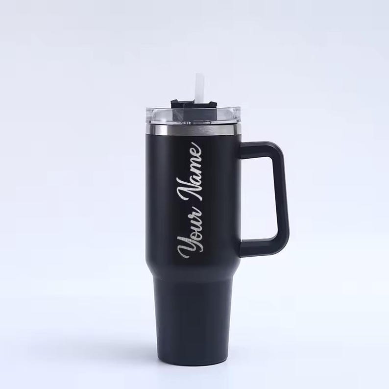 Op de afbeelding: Zwarte ge&iuml;soleerde beker met een handvat, doorzichtig deksel en rietje. De beker heeft de tekst "Your Name" in een sierlijk lettertype. Ontworpen om dranken koud of warm te houden.