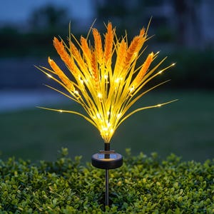 May include: A solar-powered garden light featuring a cluster of artificial golden wheat stalks illuminated by small, warm white LED lights. The light is mounted on a thin black stake with a circular solar panel base, designed for outdoor placement.