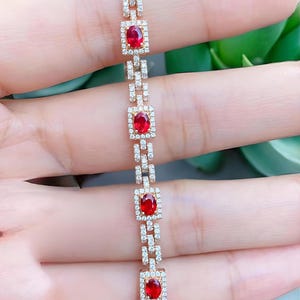 Puede incluir: Una pulsera de oro rosa con cuatro rubíes rojos de talla ovalada, cada uno centrado en un marco rectangular de pequeños diamantes blancos pavé. Los eslabones entre los engastes de los rubíes también están incrustados con pequeños diamantes.