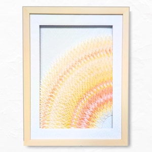 Op de afbeelding: Abstracte aquarel kunstafdruk in een licht houten frame. Het kunstwerk toont een levendig, gestructureerd ontwerp in tinten geel, oranje en perzik, dat lijkt op een gestileerde zon of lichtuitbarsting. De print is geplaatst tegen een witte passe-partout.