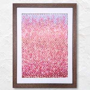 May include: A framed abstract art print featuring a textured, pink and red floral pattern that fades into a light blue hue at the top. The artwork is set within a white mat and a dark brown wooden frame.