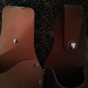 Op de afbeelding: Twee bruine leren gereedschaphouders met metalen klinknagels en een metalen clip. De houders hebben een su&egrave;de-achtige voering.