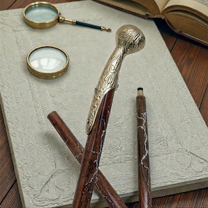 May include: A detailed image of a walking cane with a gold-colored handle and accents. The cane's shaft is a dark brown with white marbling. A magnifying glass and a small round magnifying glass are also visible.