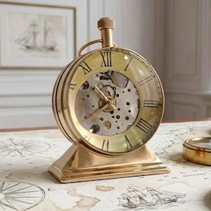 Peut inclure: Une horloge de table en métal doré avec un cadran circulaire et une couronne de remontage proéminente sur le dessus. L'horloge présente un cadran squelette révélant des engrenages argentés internes et des chiffres romains noirs sur le verre.