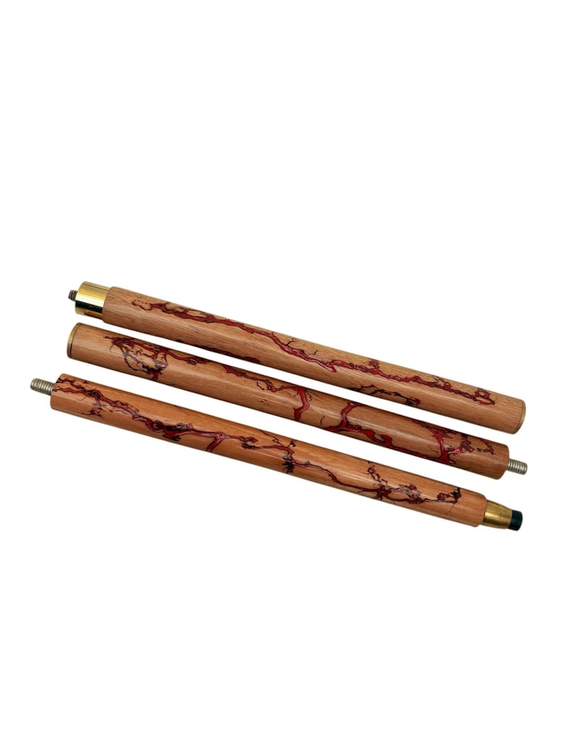 May include: Three wooden walking cane shafts with red veining and brass accents. The shafts are made of light brown wood with a natural grain pattern. The ends have metal fittings for assembly. The canes are designed for support and mobility.