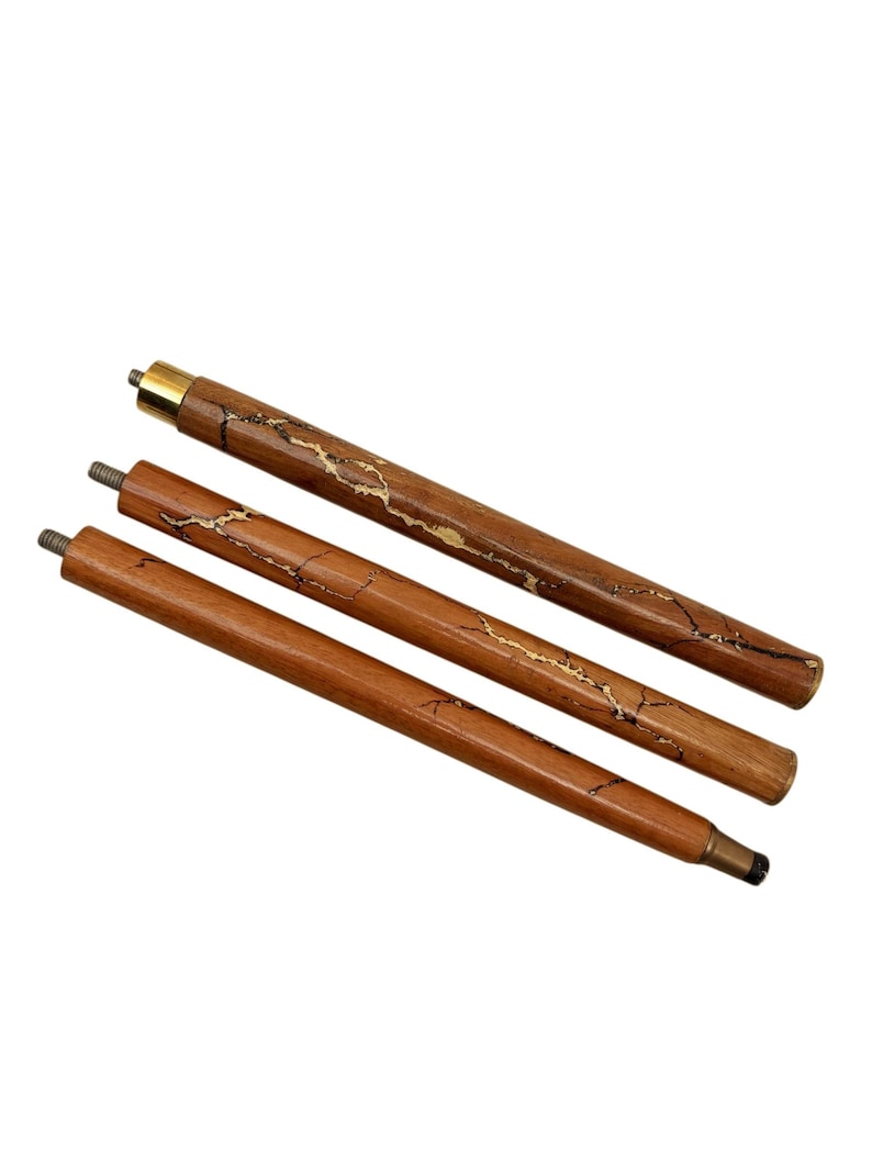May include: Three wooden walking cane replacement tips. The tips are brown with gold-colored accents. The top tip has a gold-colored metal cap. The tips are angled and have metal screw ends.