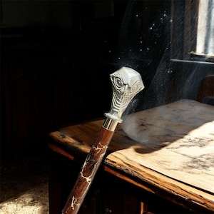 May include: A decorative walking cane with a silver-coloured, ornate head featuring an avian design. The wooden shaft is dark brown with a light-coloured, crackled pattern, and a gold-coloured band accents the top.