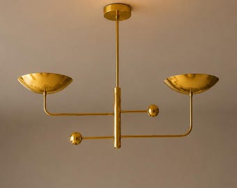 Könnte beinhalten: Eine goldfarbene, moderne Deckenleuchte mit zwei schalenförmigen Schirmen und kugelförmigen Akzenten. Die Leuchte ist an einer zentralen Stange aufgehängt und hat ein minimalistisches Design, geeignet für die Innenbeleuchtung.