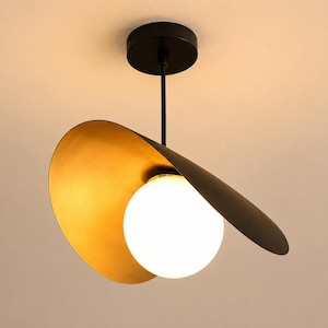 May include: Modern ceiling light fixture with a black stem and canopy. The design features a gold-colored, curved shade and a white globe light. The fixture is suspended from the ceiling, creating a contemporary aesthetic.
