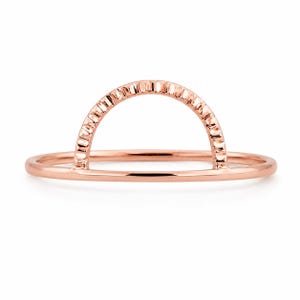 May include: A rose gold ring featuring a thin, smooth horizontal band topped with a semi-circular arch. The arch component has a textured, notched surface along its outer edge, contrasting with the polished finish of the main band.