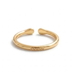May include: A gold-toned open ring featuring a smooth, polished band with rounded ends. The word Meloni is engraved in a cursive script font on the front surface of the band. The ring has a simple, continuous circular design with a small gap.