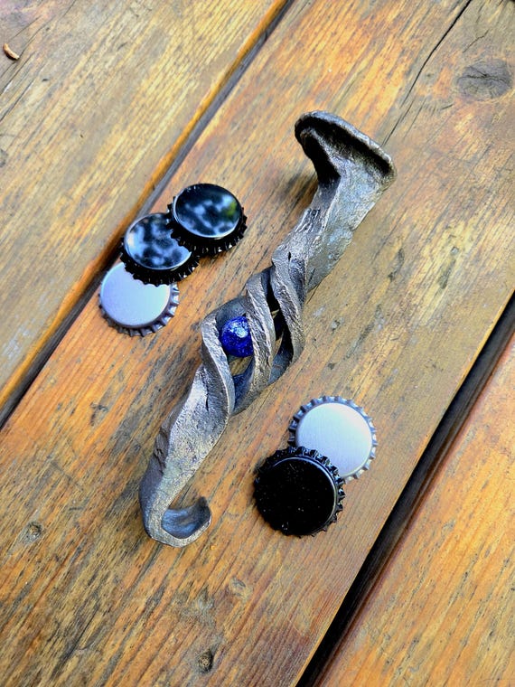 A blacksmith-forged railroad spike transformed into a bottle opener with a caged rolling marble — wildly original, genuinely one-of-a-kind, and screams 'a real craftsperson made this'.