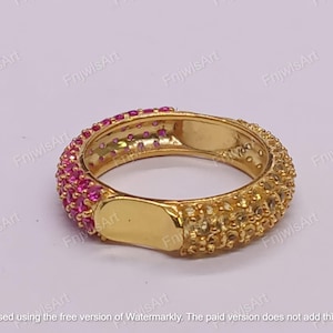 May include: A gold-colored ring with a band encrusted with small, pink gemstones on one side and textured gold on the other. The ring has a rectangular gold plate on the front.