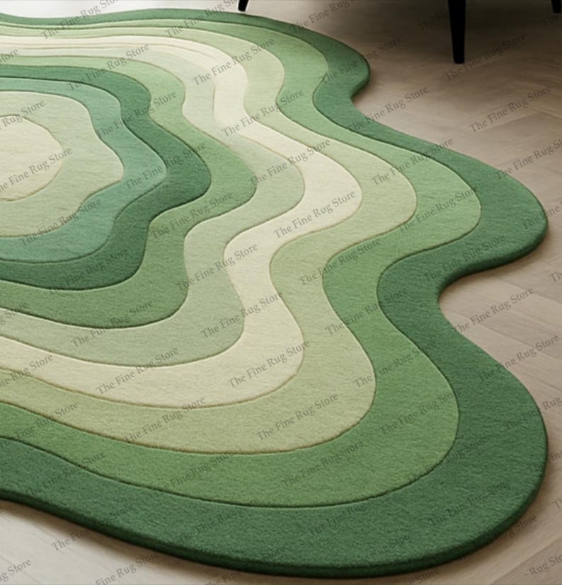 Puede incluir: Una alfombra verde con bordes ondulados y un dise&ntilde;o en capas. La alfombra presenta tonos de verde, de claro a oscuro, creando un efecto degradado. The Fine Rug Store est&aacute; impreso en la alfombra.