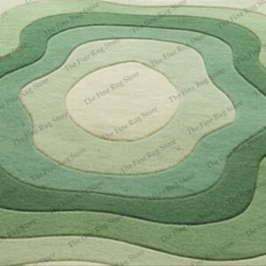 Puede incluir: Una alfombra verde y beige con un dise&ntilde;o topogr&aacute;fico en capas. La alfombra presenta l&iacute;neas conc&eacute;ntricas y onduladas en diferentes tonos de verde, creando una sensaci&oacute;n de profundidad y dimensi&oacute;n. El logotipo de The Fine Rug Store es visible.