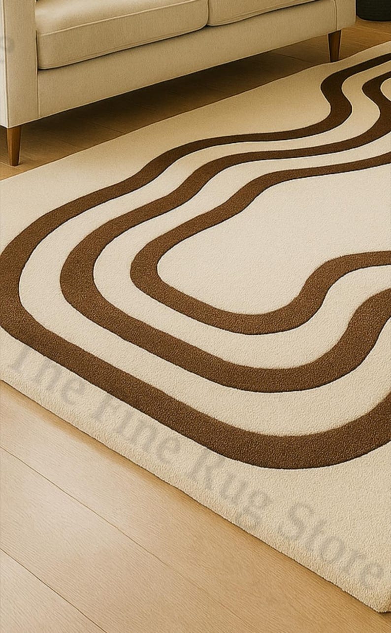 K&ouml;nnte beinhalten: Cremefarbener Teppich mit einem sich wiederholenden Muster aus wellenf&ouml;rmigen, braunen Streifen. Der Teppich liegt auf einem Holzboden, im Hintergrund ist ein beiges Sofa zu sehen. Das Design des Teppichs verleiht dem Raum eine moderne Note.