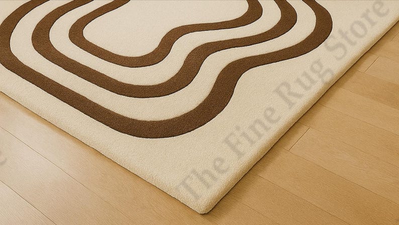 K&ouml;nnte beinhalten: Cremefarbener Teppich mit braunem, wellenf&ouml;rmigem Muster. Das Design des Teppichs weist drei geschwungene Linien auf, die einen flie&szlig;enden, organischen Look erzeugen. Der Teppich liegt auf einem hellen Holzboden, wobei die Ecke des Teppichs sichtbar ist.