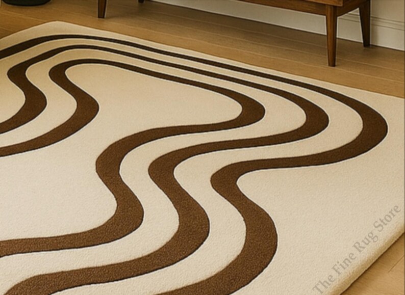K&ouml;nnte beinhalten: Ein cremefarbener Teppich mit einem sich wiederholenden braunen Wellenmuster. Der Teppich hat eine weiche Textur und ist rechteckig. Das Design erinnert an einen Retro-Stil.