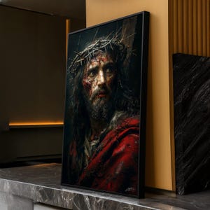 May include: A framed portrait depicts a man with a crown of thorns, bloodied face, and long dark hair. He wears a red robe. The artwork is displayed on a marble surface, with a dark background and a gold-colored wall.