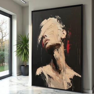 May include: Abstract portrait painting in a black frame. The artwork features a face with thick, textured brushstrokes in beige and white, obscuring the eyes. Red accents are visible on the ears. The background is black.