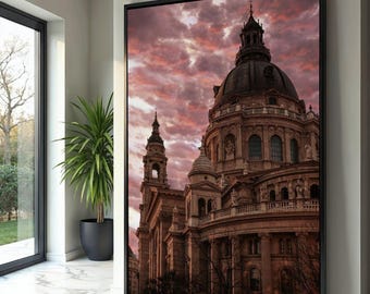 May include: A framed canvas print of a large cathedral with a domed roof and multiple spires. The building is a warm brown color, set against a dramatic sky of pink and red clouds. The print is displayed in a modern interior setting.