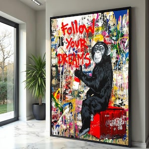 May include: Framed artwork showing a chimpanzee with a Coca-Cola can, sitting on a red Coca-Cola crate. The background is a colourful mix of graffiti and paint splatters, with the words "Follow Your Dreams" in red.