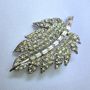 May include: A silver tone leaf-shaped brooch with clear rhinestones and baguette-shaped crystals.