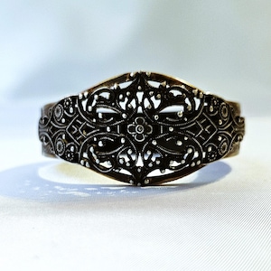 Puede incluir: Un brazalete de filigrana plateado con un delicado diseño floral. El brazalete está hecho de metal y tiene un acabado pulido.