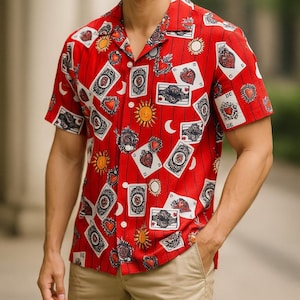 May include: Red short-sleeve shirt with a repeating pattern of playing cards, hearts, suns, and moons. The shirt has a collared neckline and vertical stripes. The shirt is worn by a person.