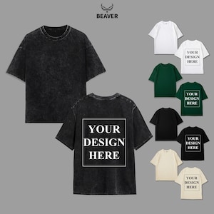 Puede incluir: Una colección de camisetas de manga corta en varios colores, incluyendo negro, blanco, verde y beige. La camiseta principal es de color gris oscuro, con un estilo lavado a la piedra. La parte trasera de la camiseta presenta el texto "YOUR DESIGN HERE" en un recuadro blanco. El logo de la marca "BEAVER" está en la parte superior.