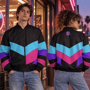 Könnte beinhalten: Eine schwarze Bomberjacke mit einem Chevron-Muster in leuchtendem Blau, Magenta und Violett auf der Brust und dem Rücken. Die Jacke hat einen durchgehenden Reißverschluss, gerippte Bündchen und eine kleine, bunte sternförmige Grafik am oberen Rücken.