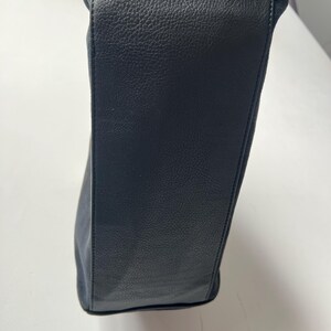 May include: A black handbag with a textured leather exterior and a suede top. The bag has a rectangular shape and appears to be empty. The stitching is visible along the seams.