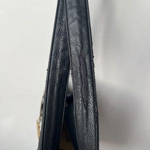 May include: Black leather shoulder bag with a textured surface. The bag's strap shows signs of wear and tear. The interior of the bag is visible, revealing a patterned fabric lining.
