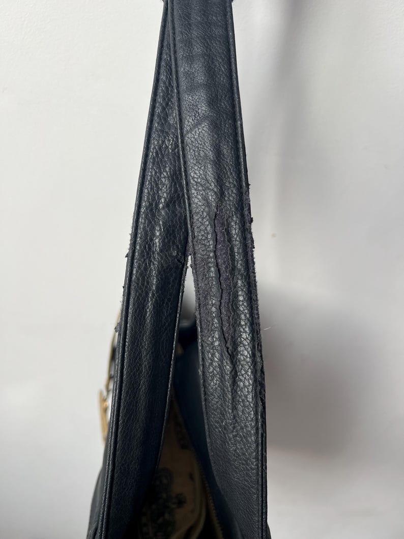 May include: Black leather shoulder bag with a textured surface. The bag's strap shows signs of wear and tear. The interior of the bag is visible, revealing a patterned fabric lining.