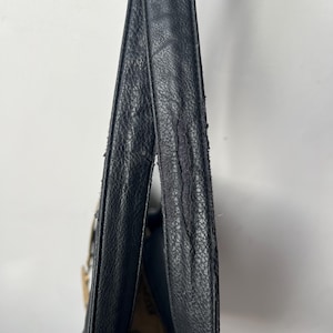 May include: Black leather shoulder bag with a textured surface. The bag's strap shows signs of wear and tear. The interior of the bag is visible, revealing a patterned fabric lining. The bag is hanging against a white background.