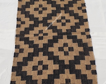 May include: Rectangular rug with a geometric pattern in black and tan. The rug has a fringed edge and a repeating design of squares and diagonal lines. The rug is made of a woven material and is suitable for home decor.