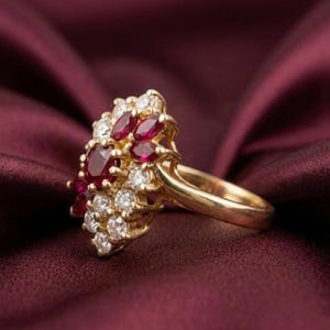 May include: A gold ring featuring a cluster of deep red marquise and round-cut rubies alongside several small, clear, round-cut white diamonds. The stones are set in a yellow gold band, creating a dense, floral-inspired arrangement of gemstones.