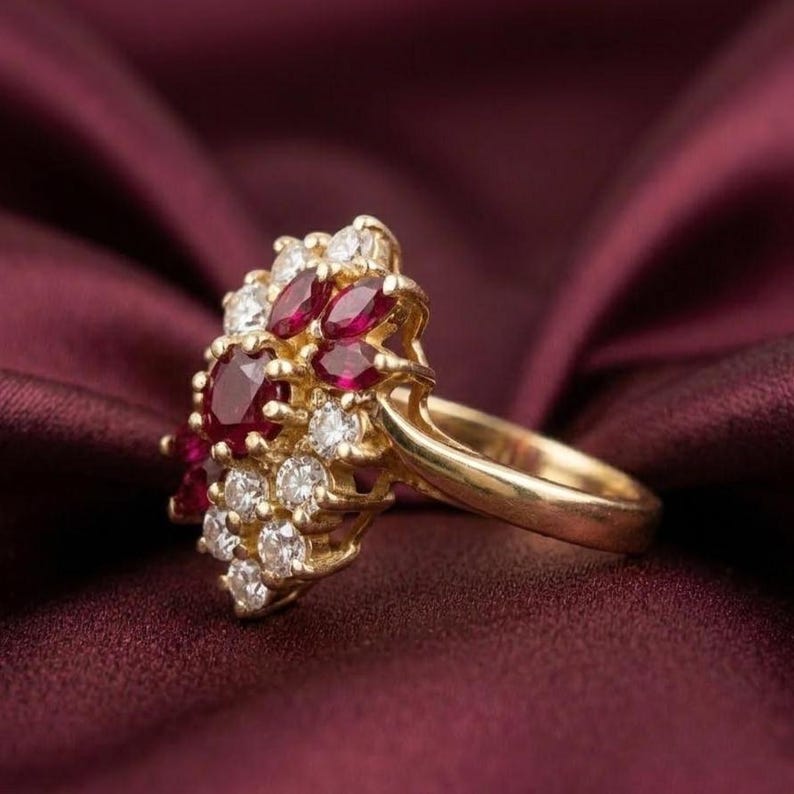 May include: A gold ring featuring a cluster of deep red marquise and round-cut rubies alongside several small, clear, round-cut white diamonds. The stones are set in a yellow gold band, creating a dense, floral-inspired arrangement of gemstones.