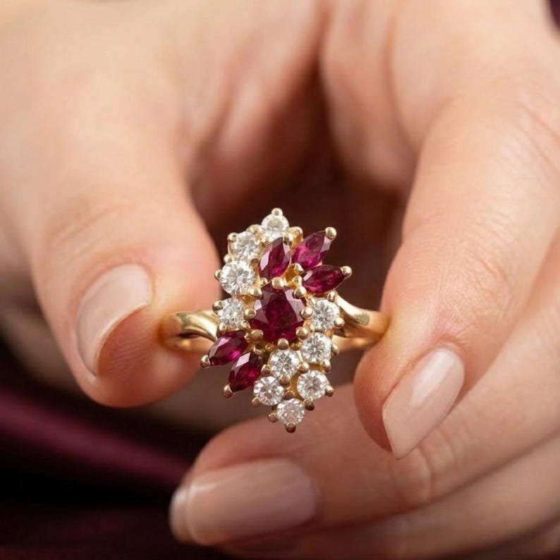 May include: A gold ring featuring a cluster of marquise-cut red rubies and round-cut white diamonds. The stones are arranged in an asymmetrical floral-inspired pattern on a polished gold band, showcasing a vibrant contrast between the red and white.