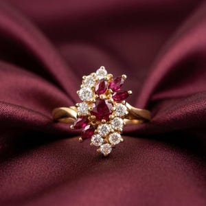 May include: A gold ring featuring a central round-cut ruby surrounded by a cluster of smaller round-cut white diamonds and marquise-cut rubies. The stones are arranged in an asymmetrical floral-inspired pattern on a polished gold band.