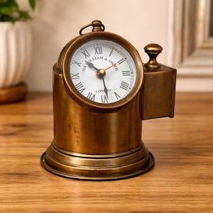 Puede incluir: Un reloj de latón antiguo con esfera blanca y números romanos negros. La esfera del reloj dice "SIR WILLIAM & SMITH LONDON". El reloj tiene un pequeño asa en la parte superior y una base decorativa. El reloj mide aproximadamente 15 cm de alto.
