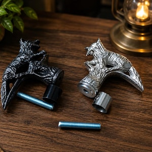 May include: Two metal cane handles shaped like a wolf perched on a tree stump, one finished in matte black and the other in polished silver. Each handle includes a matching metal collar and a threaded steel bolt for attachment to a cane shaft.