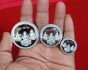 Könnte beinhalten: Drei unterschiedlich große Silbermünzen, jede mit einem geprägten Design von sitzenden Figuren und Text. Die Münzen werden in einer Hand vor rotem Hintergrund gehalten. Die größte Münze hat einen Durchmesser von etwa 3,8 cm.