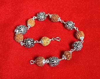 May include: A beaded bracelet with alternating silver-toned, patterned beads and brown, spherical beads. The bracelet is on a red background. The bracelet has a clasp closure.
